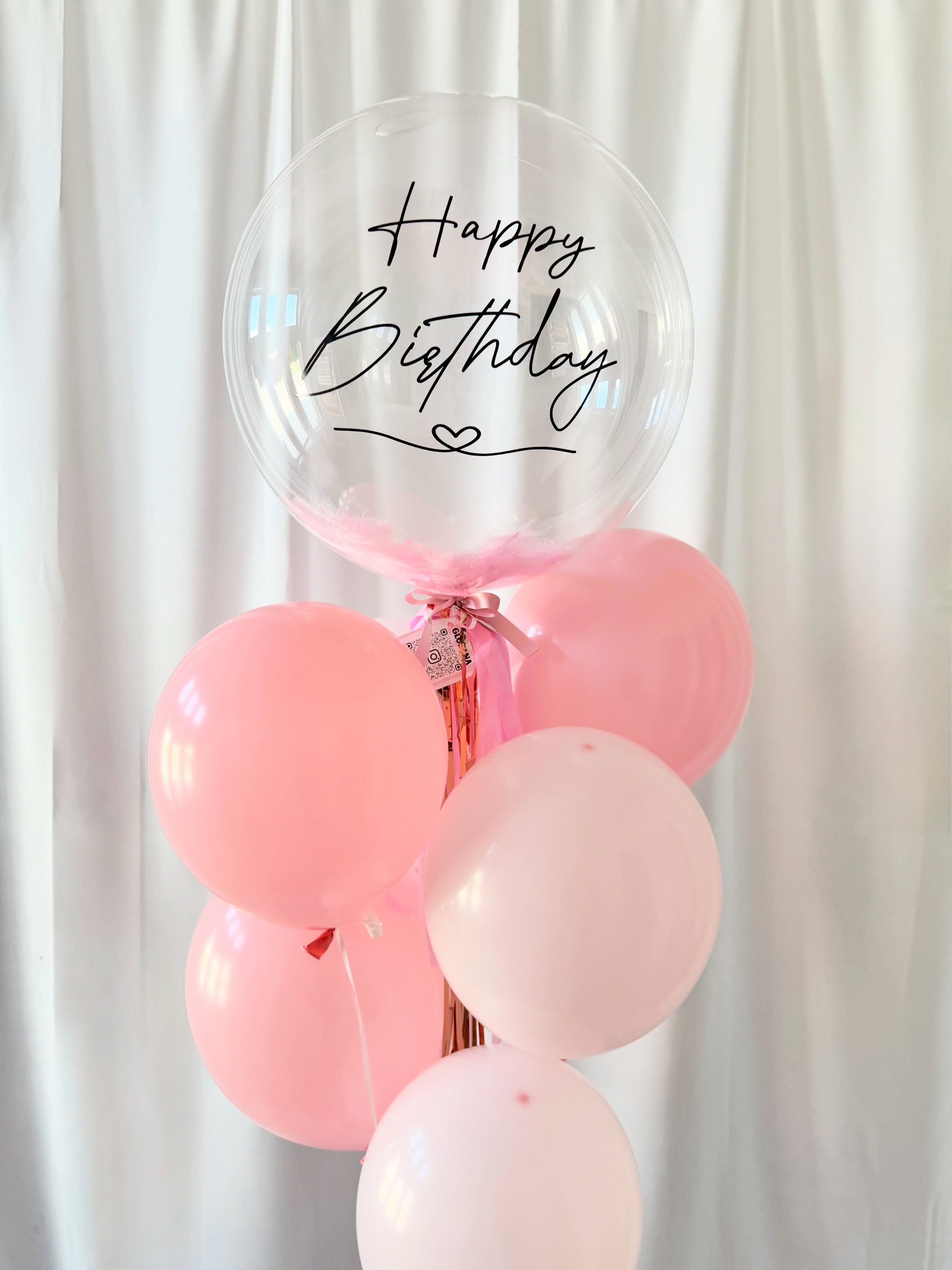 Globo burbuja de cumpleaños con plumas rosas y un bouquet de globos rosa claro.